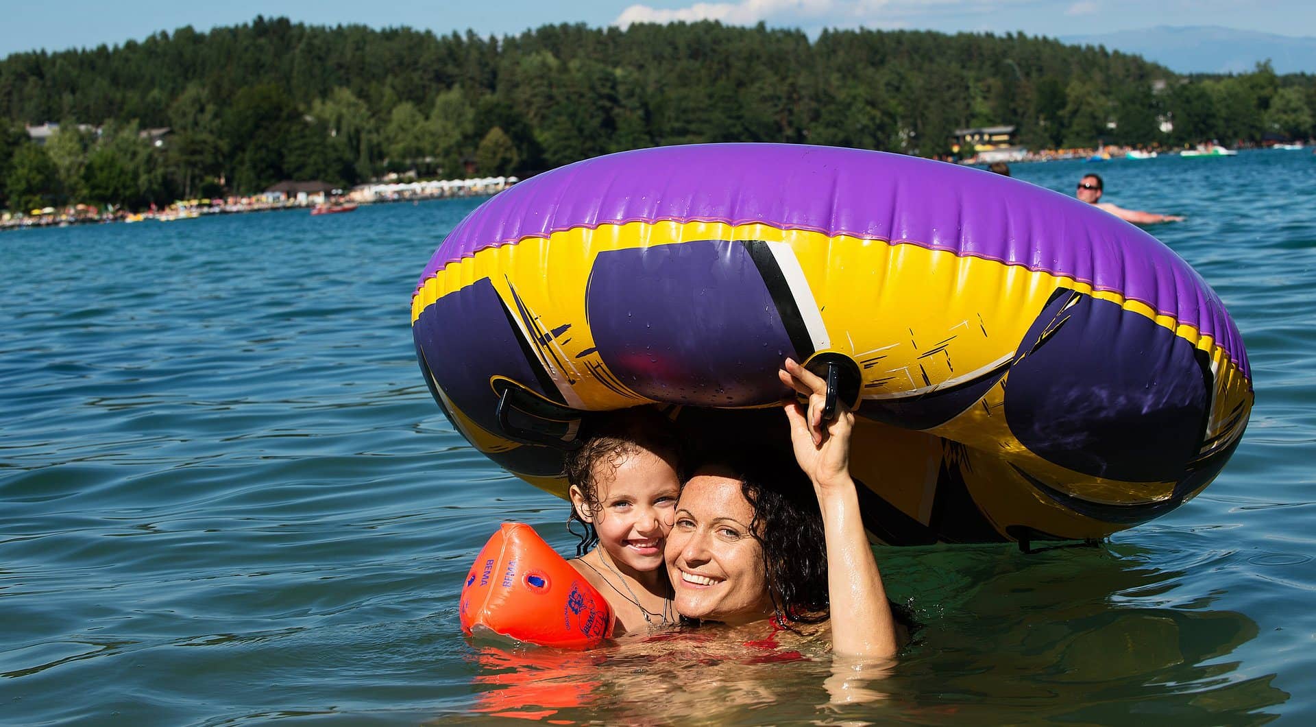 Mutter und Tochter lachen unter einem großen Schwimmreifen im Klopeiner See