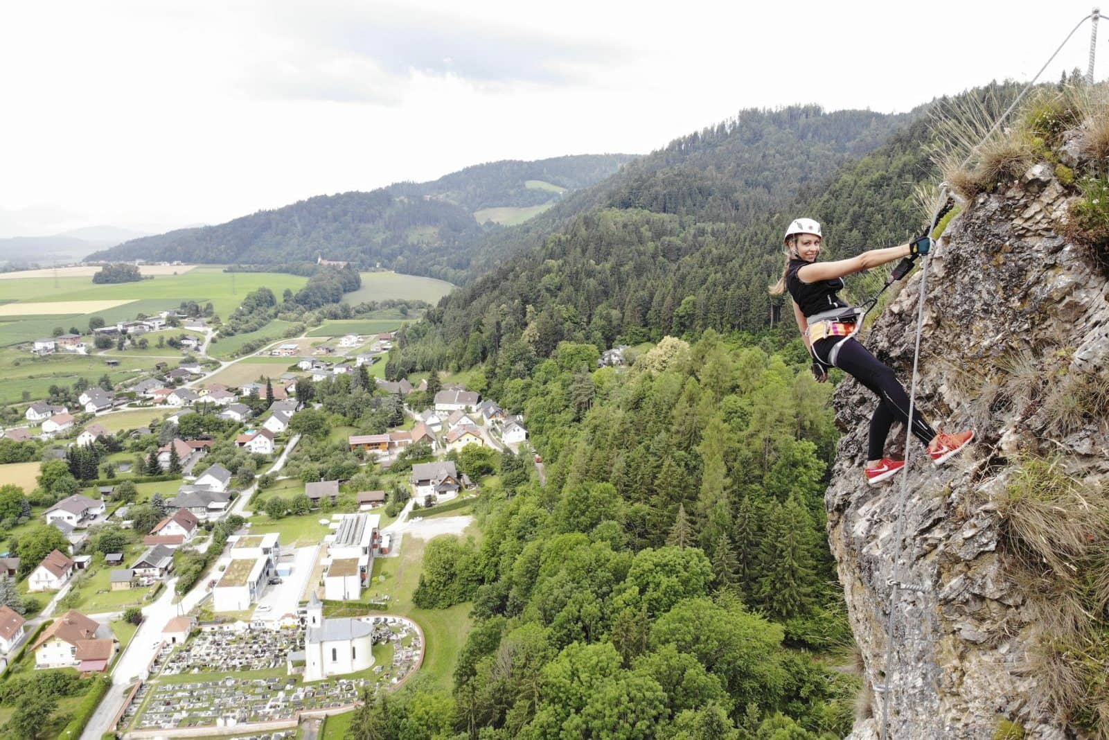 Kletterin an einer Felswand über einem Dorf