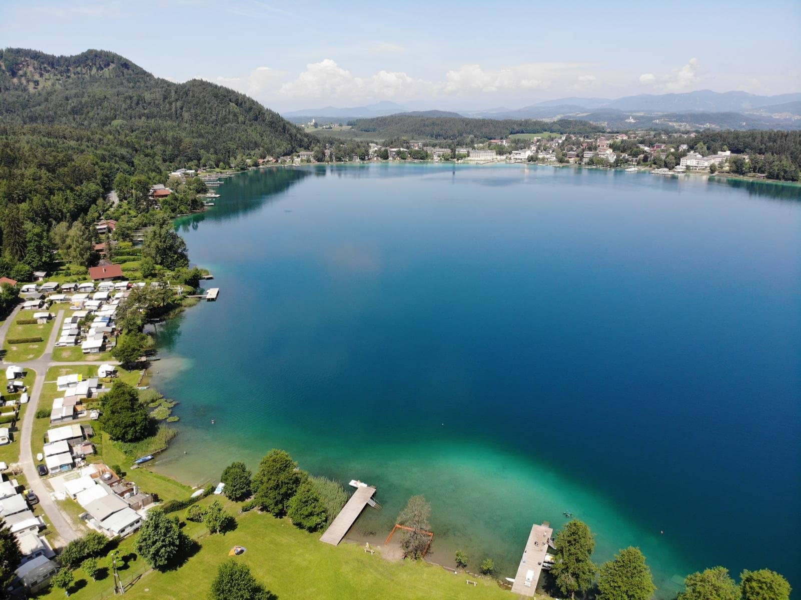 Der Klopeiner See aus der Luft mit Ufer, Stegen und Bergen im Hintergrund