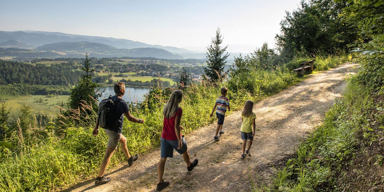 Familie wandert auf einem Waldweg mit Blick auf den See
