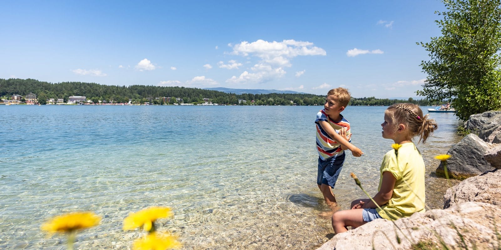 Zwei Kinder spielen im klaren, flachen Uferwasser des Klopeiner Sees
